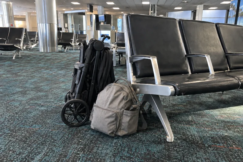 A folded stroller and a diaper bag beside gate seats