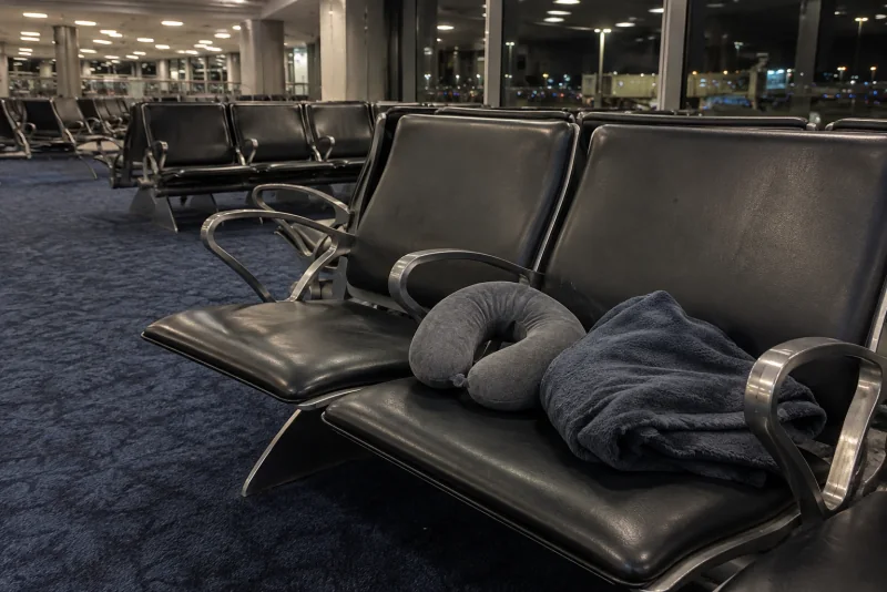 A travel pillow and blanket on gate seats at night