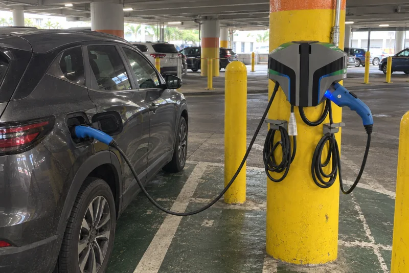 An electric car plugged into a charger on a yellow post in a parking garage
