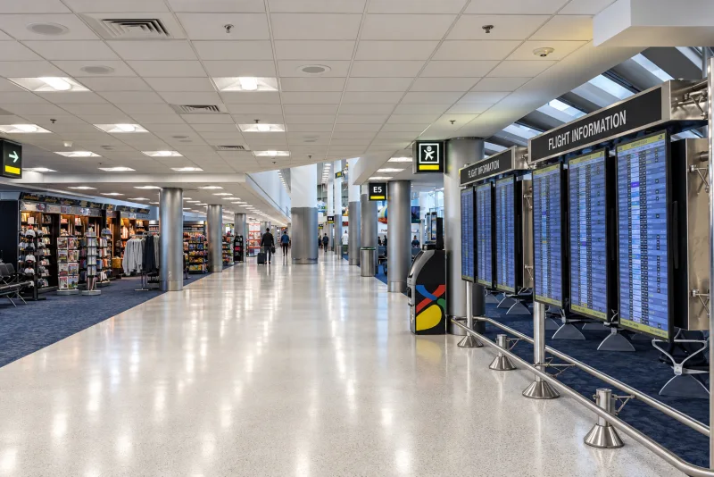 Flight information boards beside shops in a Miami airport concourse