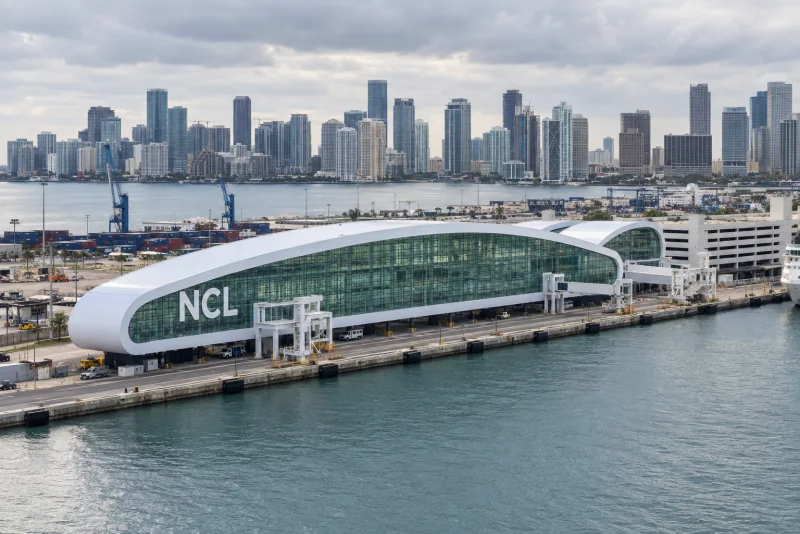 PortMiami's white, curved Cruise Terminal B beside the channel, the downtown skyline behind
